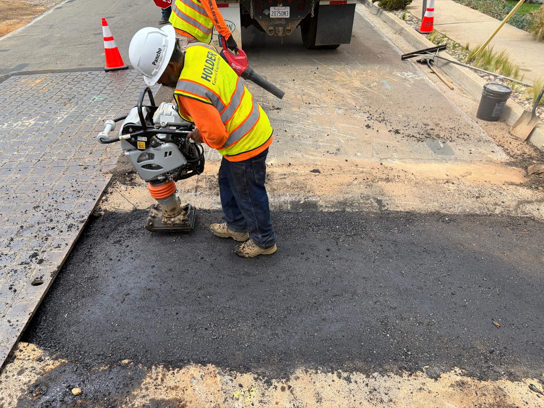 A Holder crew member in hi-vis gear running a plate compactor on fresh asphalt.