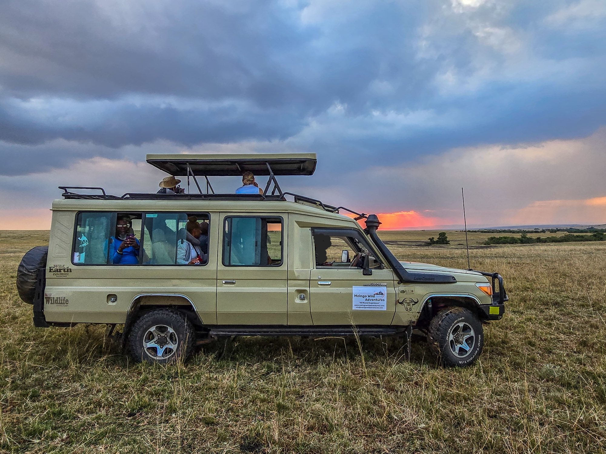A Mzingo safari vehicle on the open savannah under a stormy sunset sky.