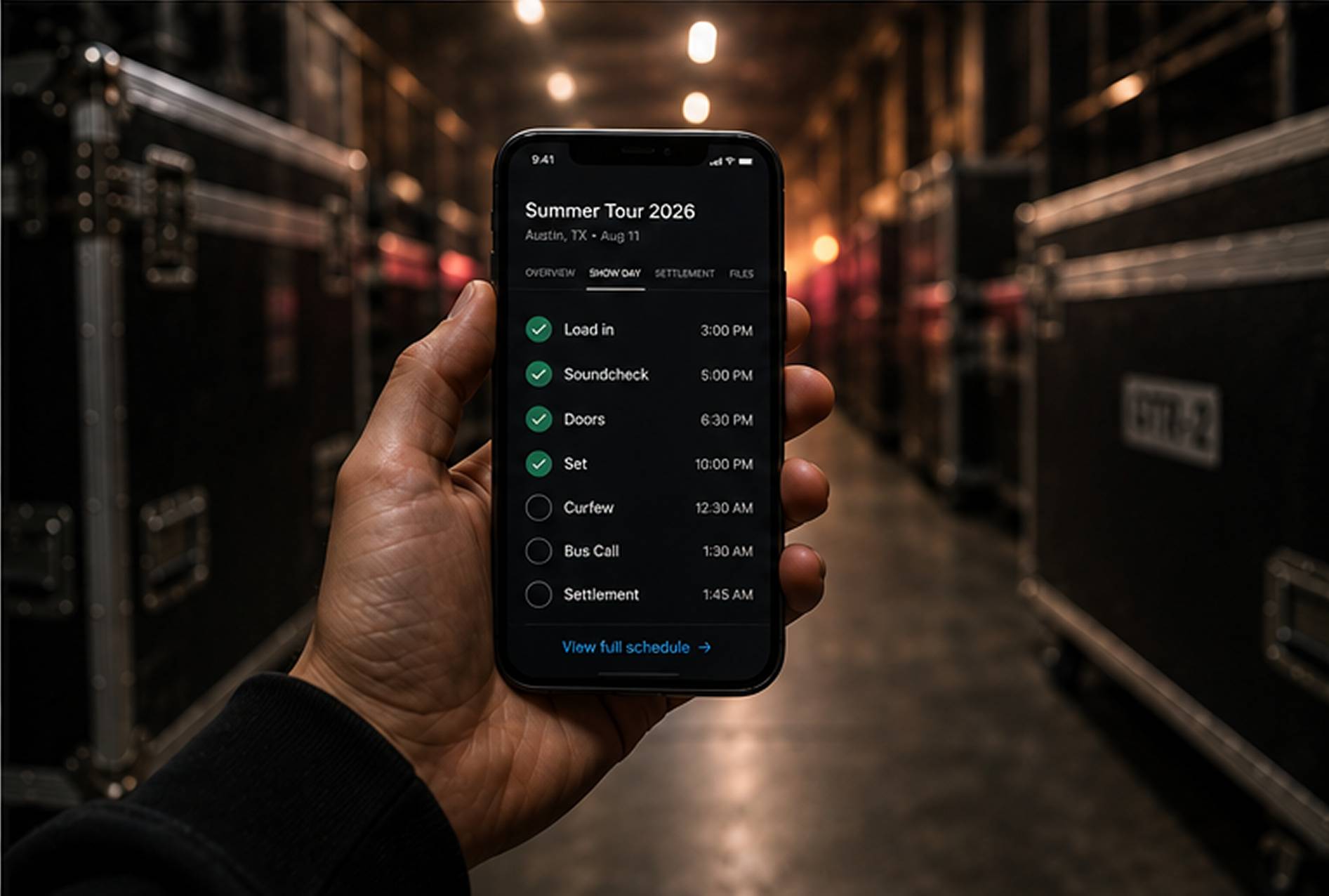 A hand holding a phone showing the TourMode show-day schedule in a dark backstage corridor.
